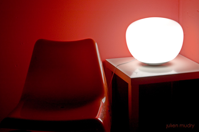 Une chaise, rouge, une sphère lumineuse, blanche, un mur, rouge.