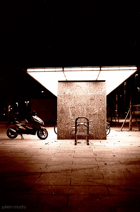 Un parc à vélos de nuit, avec un seul scooter.
