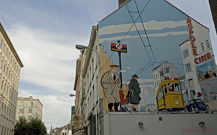 Fresque murale à Bruxelles, dessinée par Chaland, trois personnages attendant à un arrêt de tram devant un cinéma.