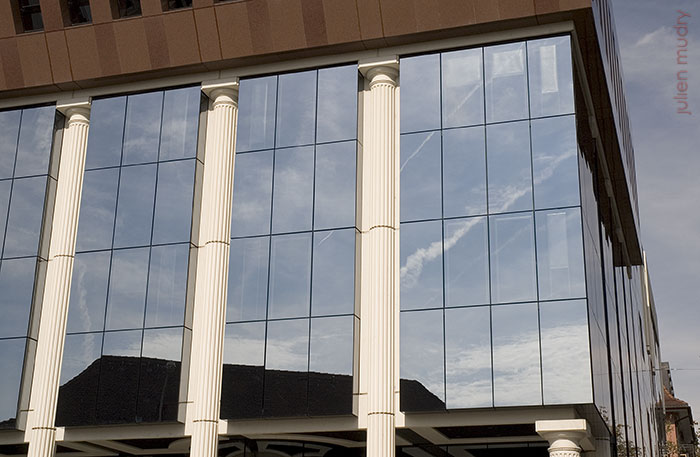Un bâtiment moderne, entièrement en verre miroir et avec des colonnes de temple grec.